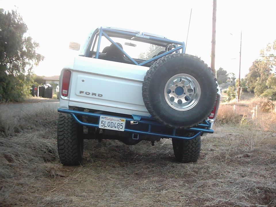 Rear view of white 1978 Ford Bronco with blue roll cage and spare tire
