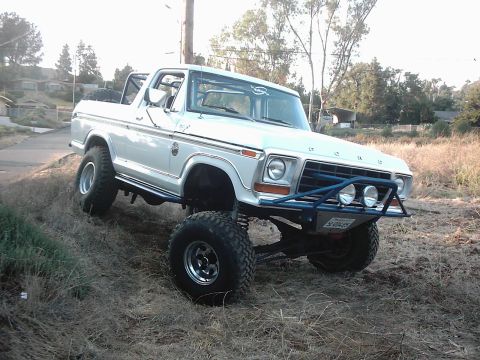 1978 Ford Bronco - 1978 Ford Bronco with custom blue front bumper and off-road tires, tilted on a grassy incline.