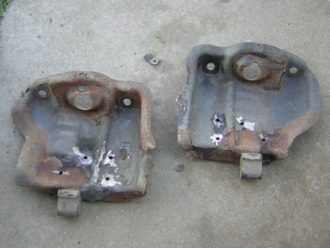 1995 Ford Bronco - Two heavily rusted metal undercarriage parts with drilled holes are shown on a concrete surface.