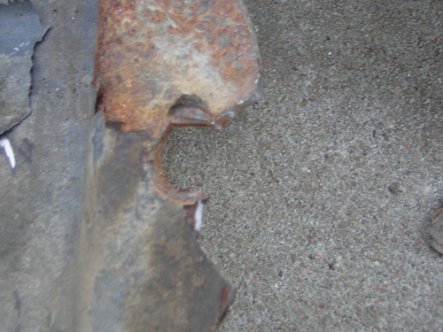 close-up of a heavily rusted, damaged metal piece with peeling paint and a jagged edge