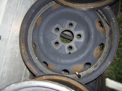 1995 Ford Bronco - A single rusty steel wheel rim is shown, with other rims stacked nearby.