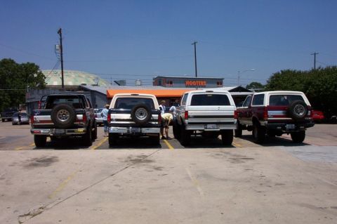 1992 Ford Bronco - Rear view of four full-size Ford Broncos backed into adjacent parking spaces at a club meet outside a Hooters, three of them carrying swing…