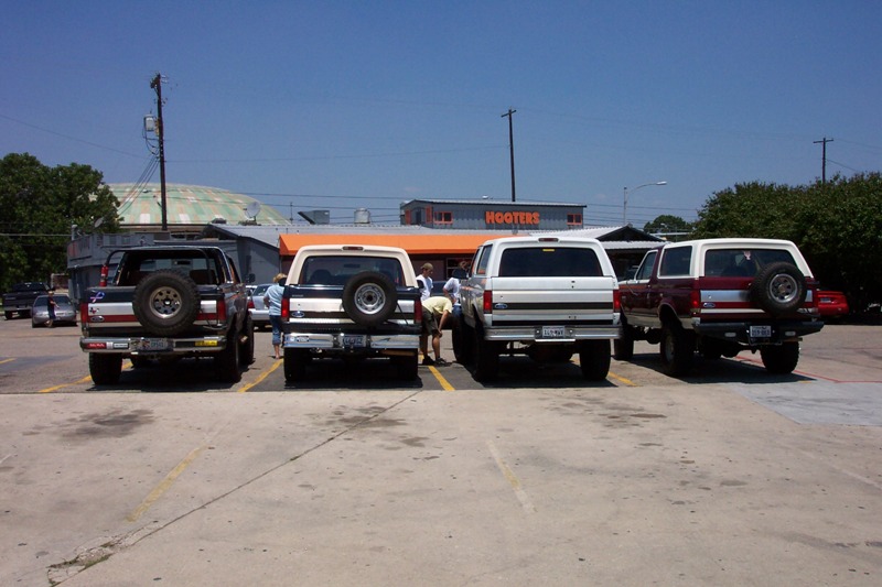 Four Ford Broncos parked rear-facing in a row outside a Hooters restaurant