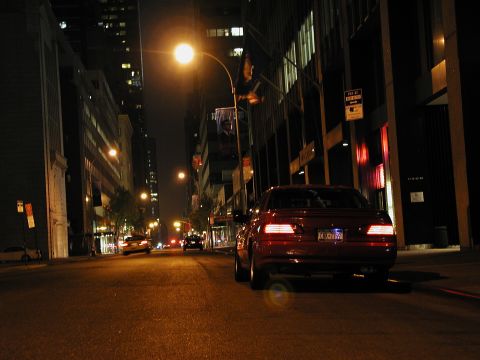 1992 Ford Taurus - Red 1992 Ford Taurus driving through a city at night, with other vehicles on the road.