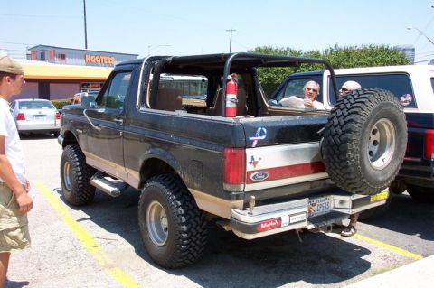 1992 Ford Bronco - Rear three-quarter view of a lifted black-over-tan Ford Bronco with its hardtop removed, showing an interior roll bar, a fire extinguisher…