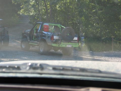 1995 Ford Bronco - A modified Ford Bronco with a green roll cage is parked on a dirt road, with another vehicle partially visible to the left.