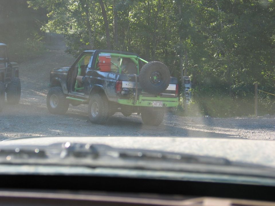 Black Ford Bronco with green roll cage and spare tire on rear, seen from behind