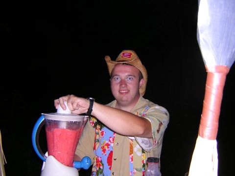 1995 Ford Probe - A man wearing a cowboy hat and a Hawaiian shirt prepares a blended drink outdoors at night.