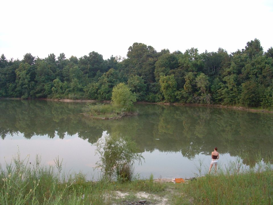 Water reflects trees and sky at a lake with a person standing on the bank