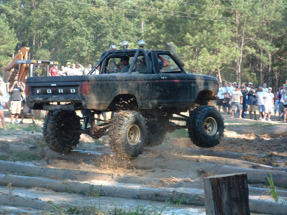Ford Bronco jumping over logs in mud pit, crowd watching