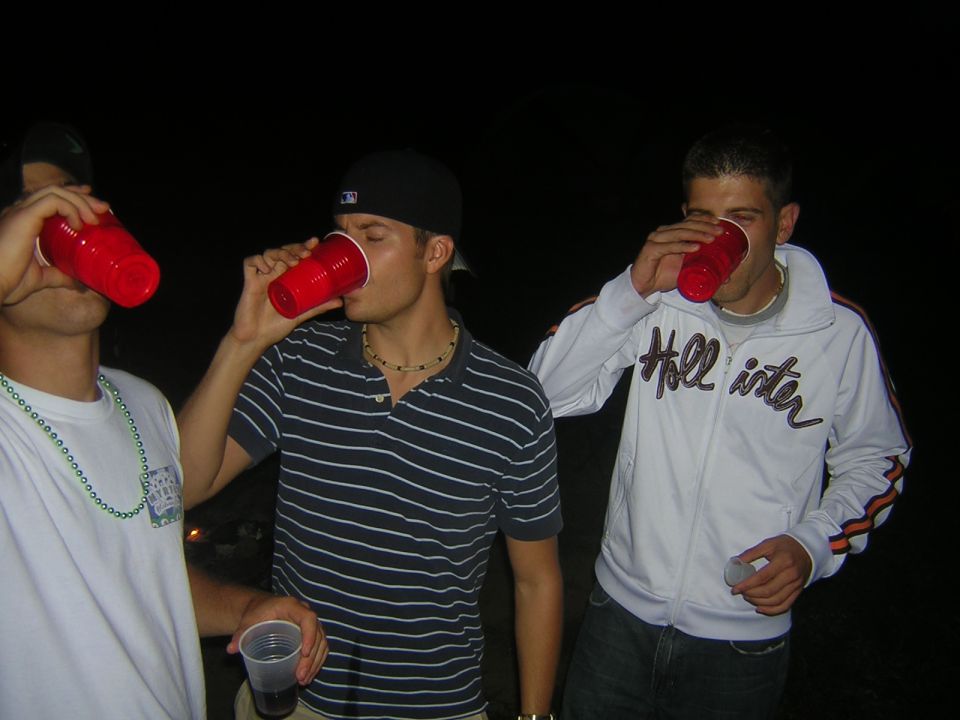 Three men drinking from red cups at night