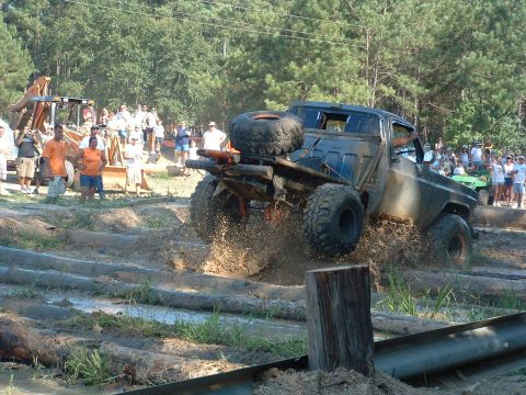 1993 Ford Bronco - An off-road truck navigates a challenging course of logs and mud, with spectators watching.