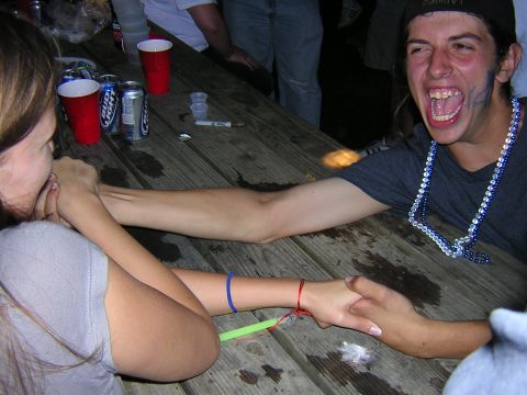 1995 Ford Probe - Two individuals engage in an arm wrestling match at a wooden picnic table, surrounded by party elements like red cups and beer cans.