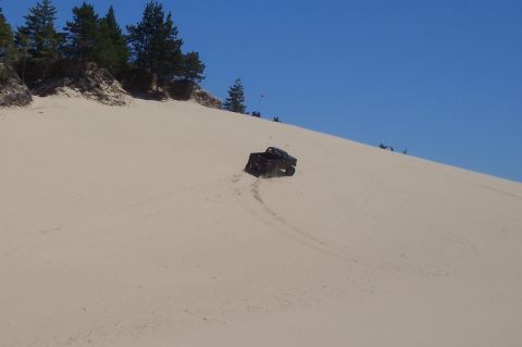 1994 Ford F-150 - A dark-colored truck navigates a sandy slope under a clear blue sky.