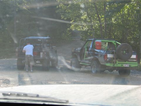 1995 Ford Bronco - Two off-road vehicles are stopped on a dusty trail, with one being loaded by a person.