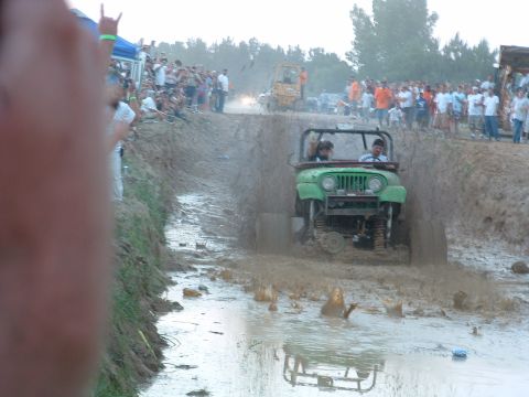 1993 Ford Bronco - Spectators watch as a green jeep navigates a muddy obstacle course.