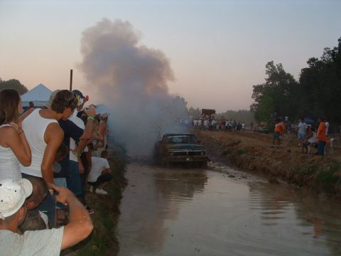 1993 Ford Bronco - Spectators watch a truck power through a muddy track, kicking up water and smoke.