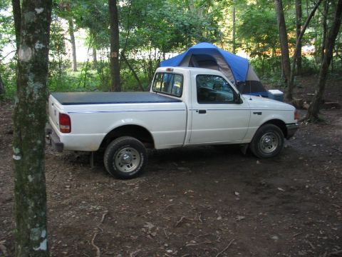 1995 Ford Bronco - A white pickup truck is parked in a campsite with a blue tent behind it.