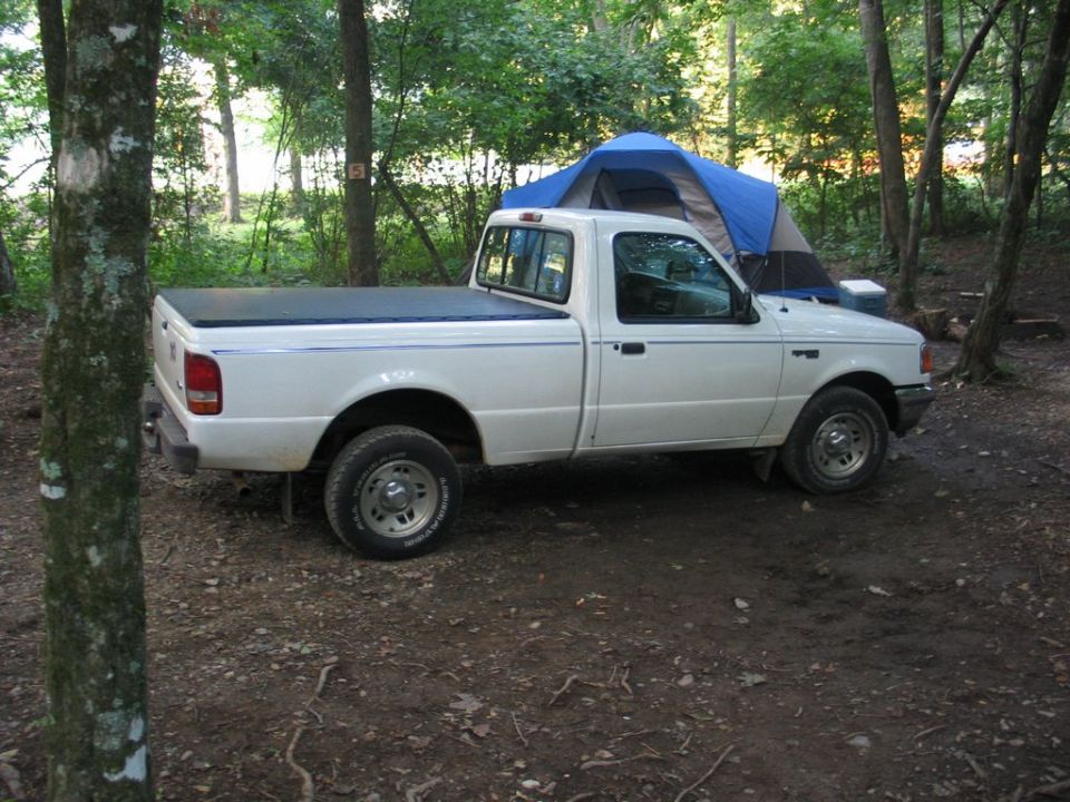 White pickup truck parked in a wooded area next to a blue tent