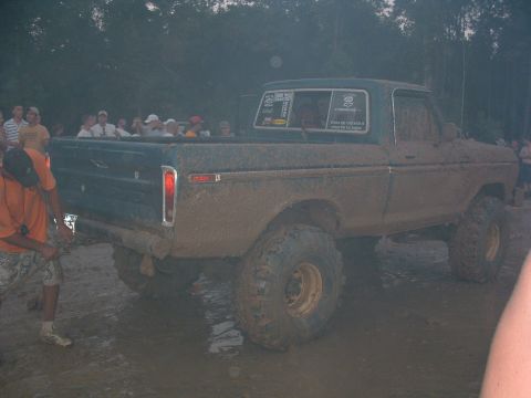 1993 Ford Bronco - Muddy pickup truck with people in the bed during an event.