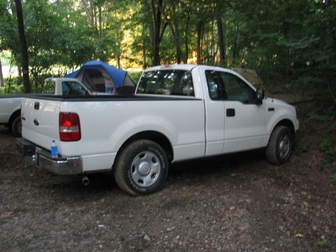 1995 Ford Bronco - A white pickup truck is parked in a campsite with a tent set up nearby.
