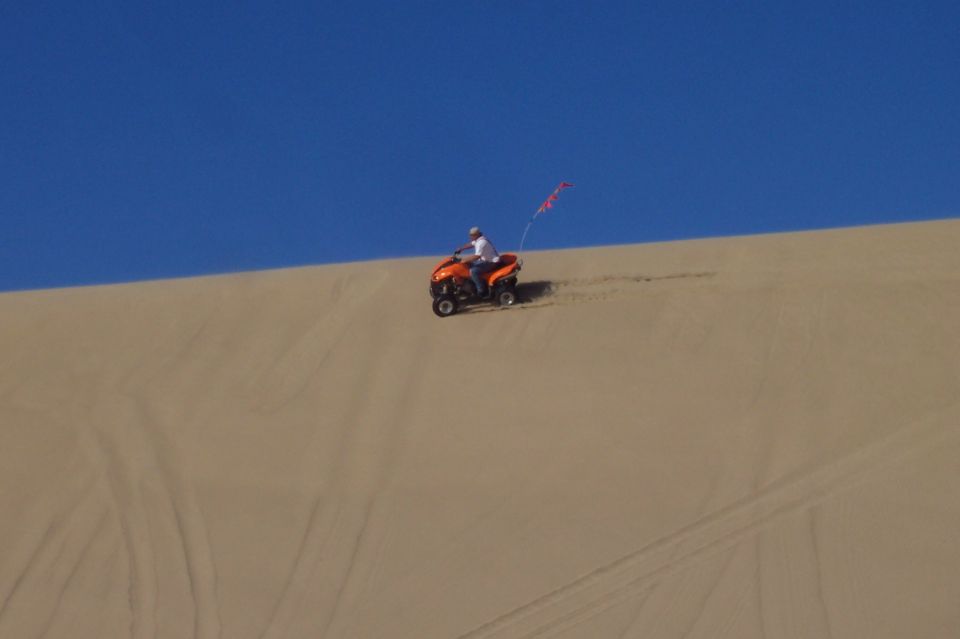 Orange ATV with rider on a sand dune under a blue sky