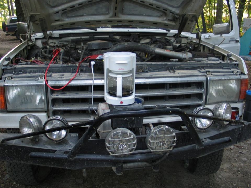 White pickup truck, hood open, showing engine. Coffee maker sits on the grille. Aftermarket bumper with lights