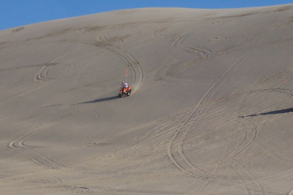 Orange ATV with rider on sand dune, leaving tire tracks