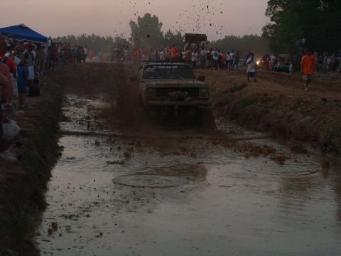 1993 Ford Bronco - A Ford Bronco navigates a muddy obstacle course during an event with a crowd gathered to watch.