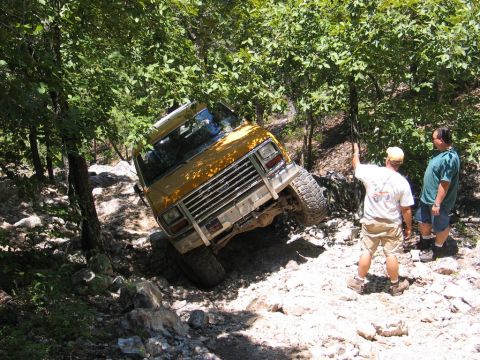 1995 Ford Bronco - A yellow off-road vehicle navigates a challenging rocky trail with two people observing.