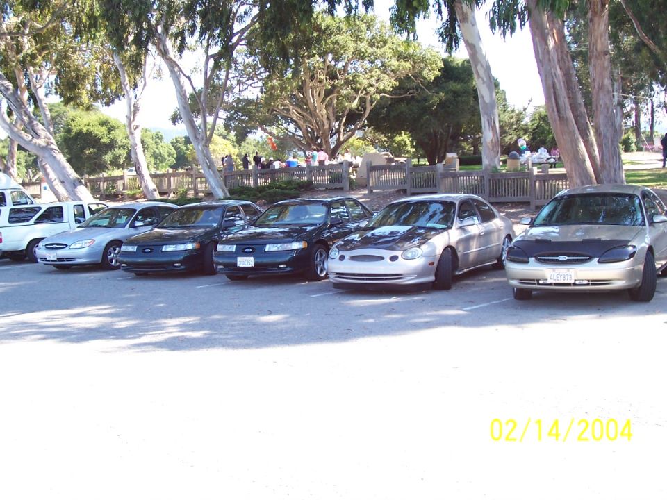 Silver sedan with aftermarket hood and custom grille, parked in a line with other cars