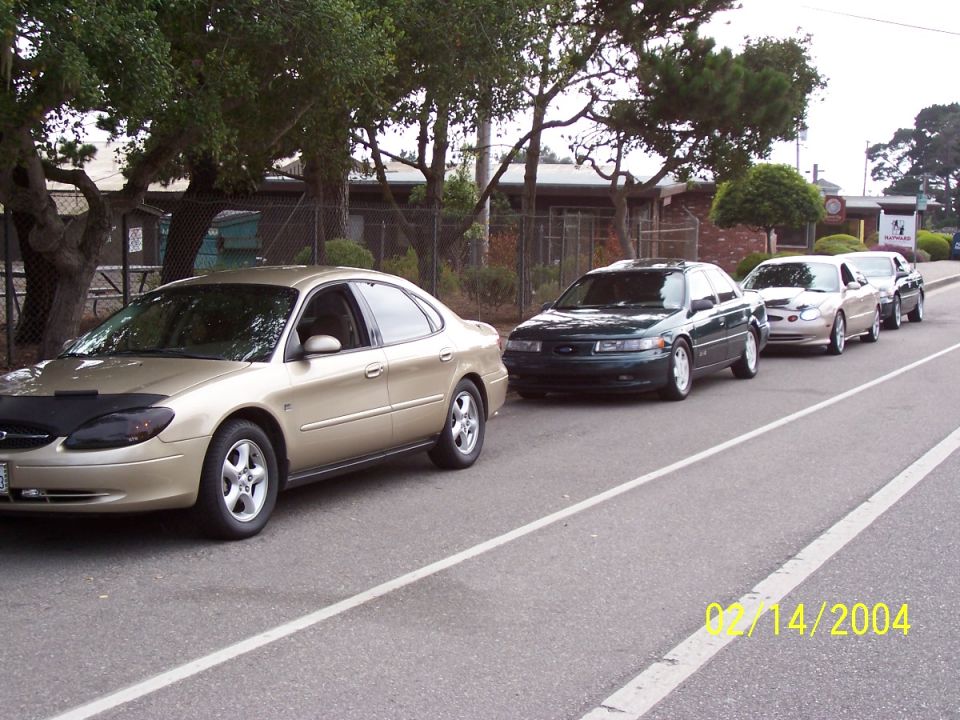 Four sedans parked in a line on a street, one with a car bra. Date stamp reads 02/14/2004