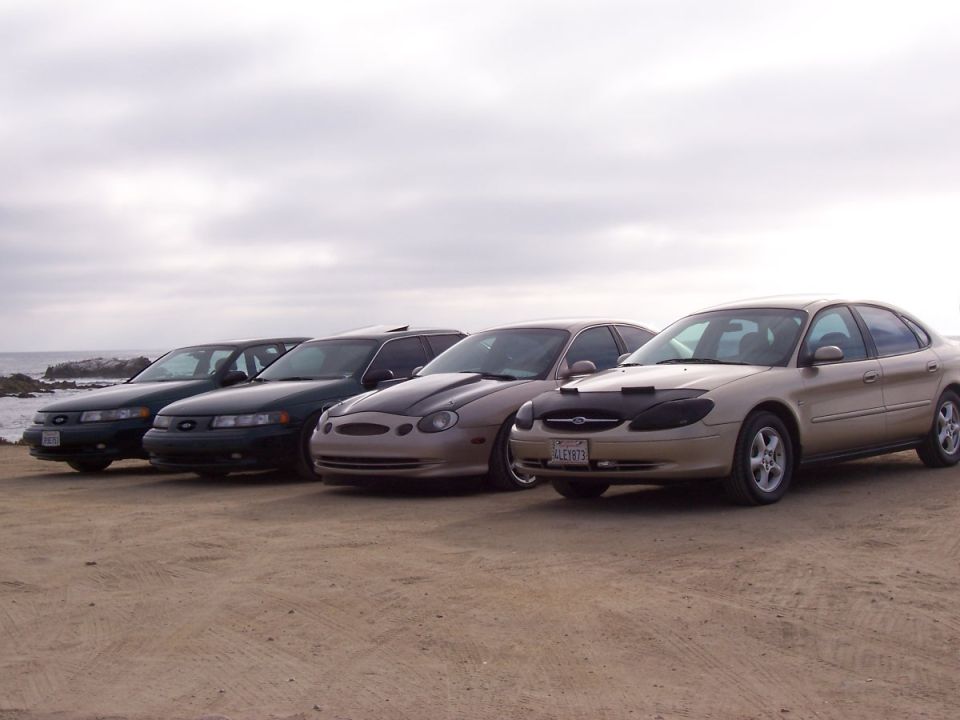 Four sedans parked on a beach, one is a 1998 Mercury Sable