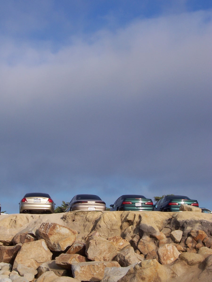 four sedans parked on a rocky ledge under a cloudy sky