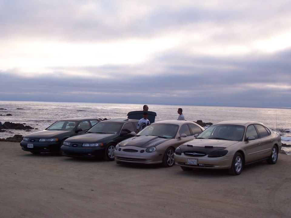 Four 1998 Mercury Sables parked on a beach with the ocean in the background