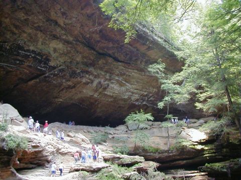 1994 Ford Probe - People explore a large cave entrance surrounded by trees and rock formations.