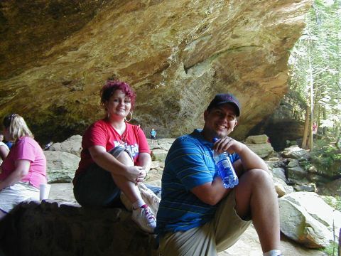 1994 Ford Probe - Two people relax in a cave, with a rock formation overhead and trees in the background.