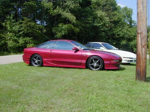 1994 Ford Probe - Two cars are parked on a grassy area with trees behind them. A wooden pole stands to the right.