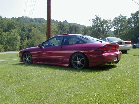 1994 Ford Probe - A maroon 1994 Ford Probe is parked on a grassy area with trees in the background.