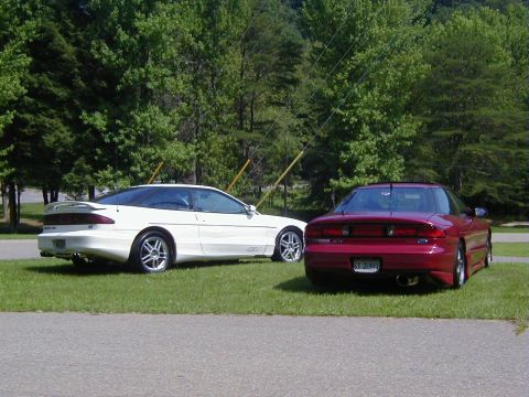 1994 Ford Probe - Two Ford Probes, one red and one white, are parked on a grassy area with trees in the background.