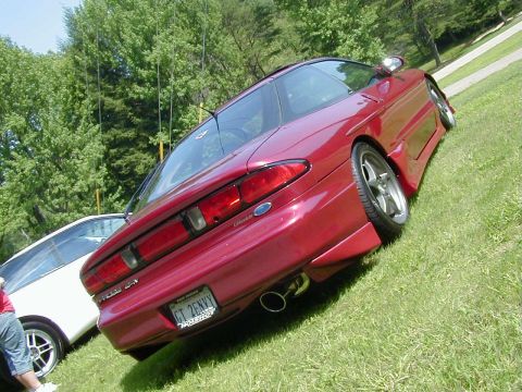 1994 Ford Probe - A red coupe is parked on a grassy slope, showing its rear end and custom license plate.
