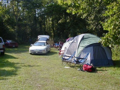 1994 Ford Probe - A white 1994 Ford Probe is parked at a campsite with tents and people relaxing nearby.