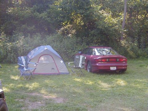 1994 Ford Probe - A red coupe is parked in a grassy area with a tent and chairs nearby.