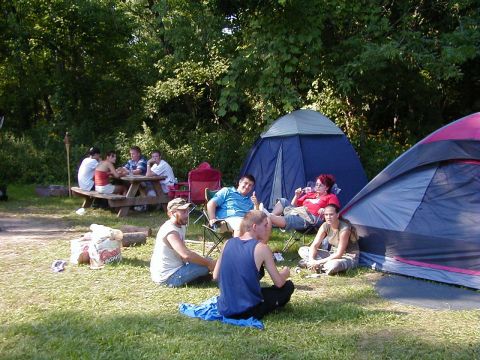 1994 Ford Probe - A group of friends enjoy a camping trip, relaxing by tents and a picnic table in a wooded area.