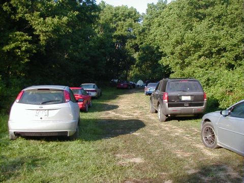 1994 Ford Probe - A collection of vehicles are parked along a wooded dirt road.