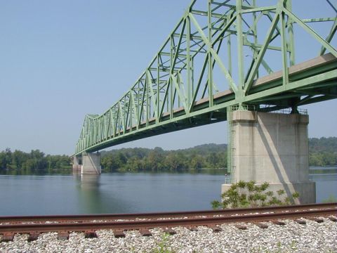 1994 Ford Probe - A large green bridge spans a calm river under a clear blue sky, with railroad tracks visible in the foreground.