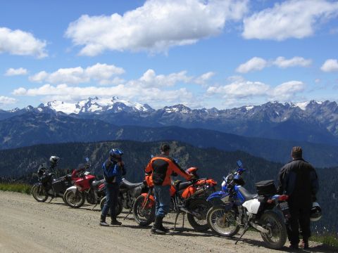 1997 BMW F650 - Several motorcycles are parked on a dirt road with a mountain range under a cloudy blue sky.