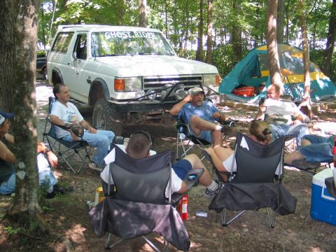 1995 Ford Bronco - A group of people relax around a campsite with a modified Ford Bronco in the background.