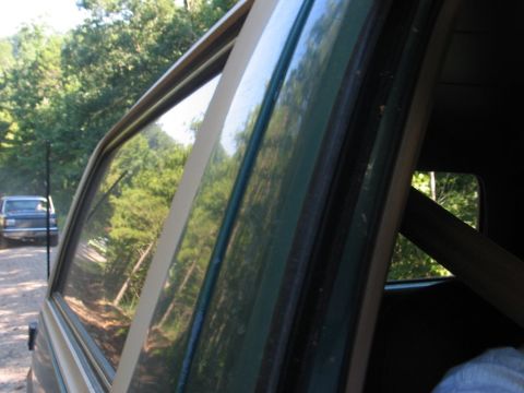 1995 Ford Bronco - A dark blue Ford Bronco is visible on a dirt road, seen through the window of another vehicle.