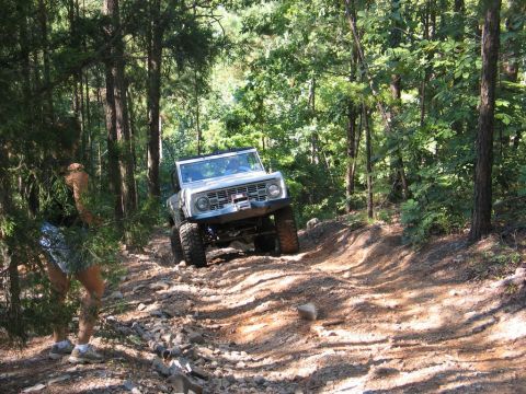 1995 Ford Bronco - A white Ford Bronco navigates a challenging rocky trail through a wooded area.